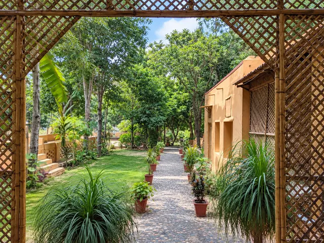 Bamboo lattice gateway opening onto a pebble garden pathway lined with potted plants at Roopam Resort, Ranakpur