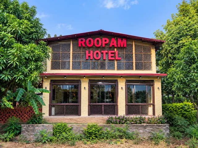 Front view of Roopam Resort in Ranakpur by day, a two-storey brick building with large windows surrounded by green trees